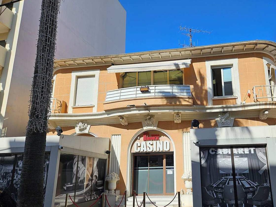 Façade du casino Partouche de Juan-les-Pins, une villa ocre avec l'enseigne Casino au-dessus de l'entrée, encadrée de deux terrasses vitrées