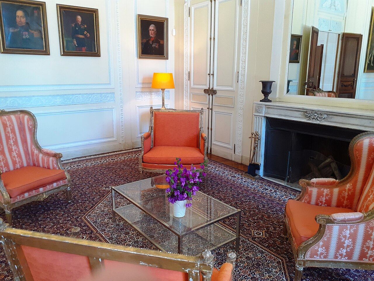 Un salon de la villa Eilenroc, fauteuils orange, cheminée de marbre et portraits aux murs